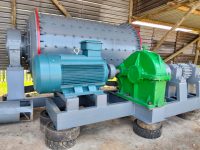 Industrial machinery in a workshop with a large gray cylindrical component, a blue motor, and a green gearbox. The setting is rustic and functional.
